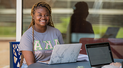 Female smiling sitting outside with laptop.