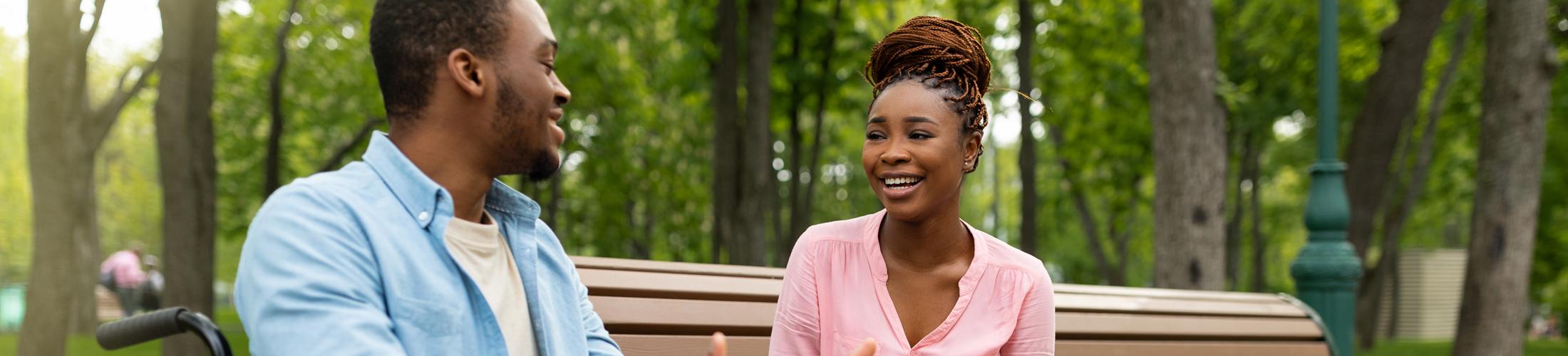 A woman talking to man in a wheelchair in the park.